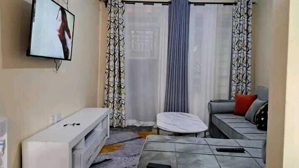 Un salon avec un canapé, une petite table, un téléviseur fixé au mur et des rideaux à motifs.