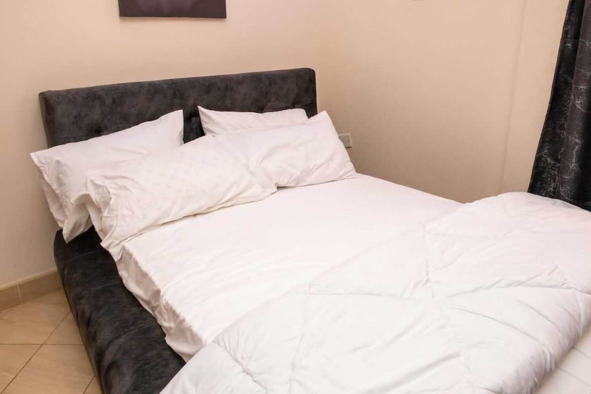 A bed with a dark headboard and white bedding in a room with beige walls and a tiled floor.