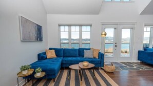 Una sala de estar moderna con un sofá seccional azul, una mesa de centro redonda y un ventanal con vistas al mar.