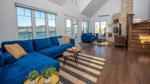 Un salón amplio con un sofá azul, una chimenea y ventanas grandes que dan al exterior.
