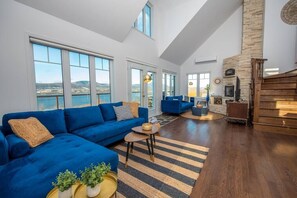 A spacious living room with a blue sofa, a fireplace, and large windows offering a view of the outdoors.