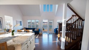 Una cocina amplia con una isla grande, un área de comedor con un sofá azul y vistas a un lago a través de las ventanas.