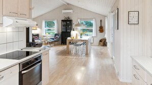 Une cuisine spacieuse avec un plafond haut, un coin repas avec une table et des chaises, et une vue sur l’extérieur grâce à de grandes fenêtres.