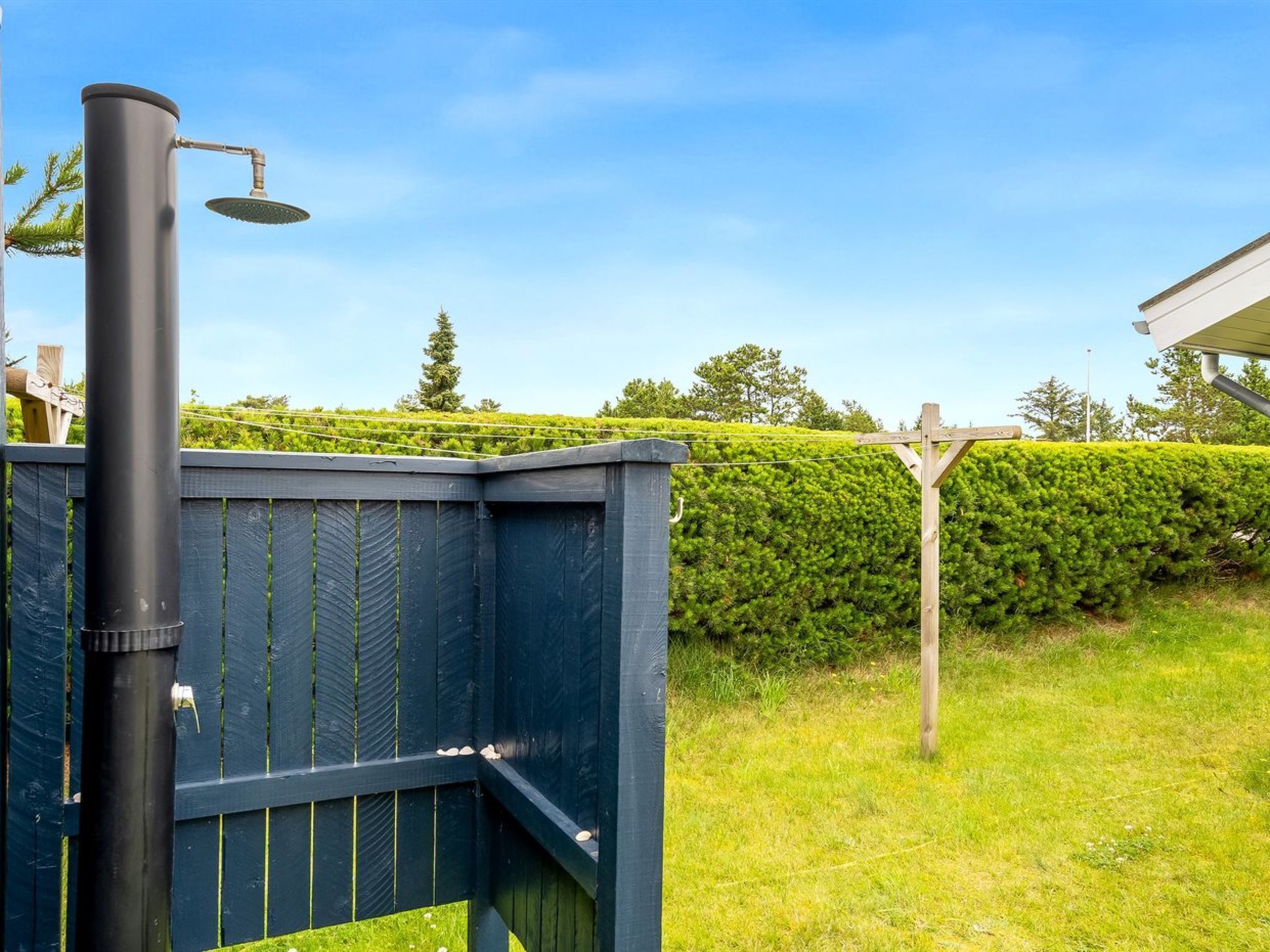 A black metal structure with a showerhead, a wooden fence, and a well-maintained hedge in a garden setting.