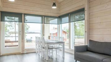 Een ruime kamer met een eettafel en stoelen, een grijze bank en grote ramen met uitzicht op het landschap.