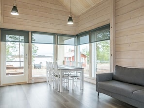 Une pièce spacieuse comprenant une table à manger et des chaises, un canapé gris et de grandes fenêtres donnant sur l’extérieur.