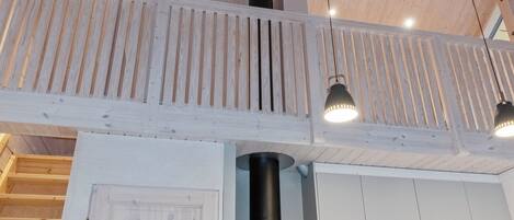 Een houten interieur met een balkon, een zwarte cilindervormige kolom en hanglampen.