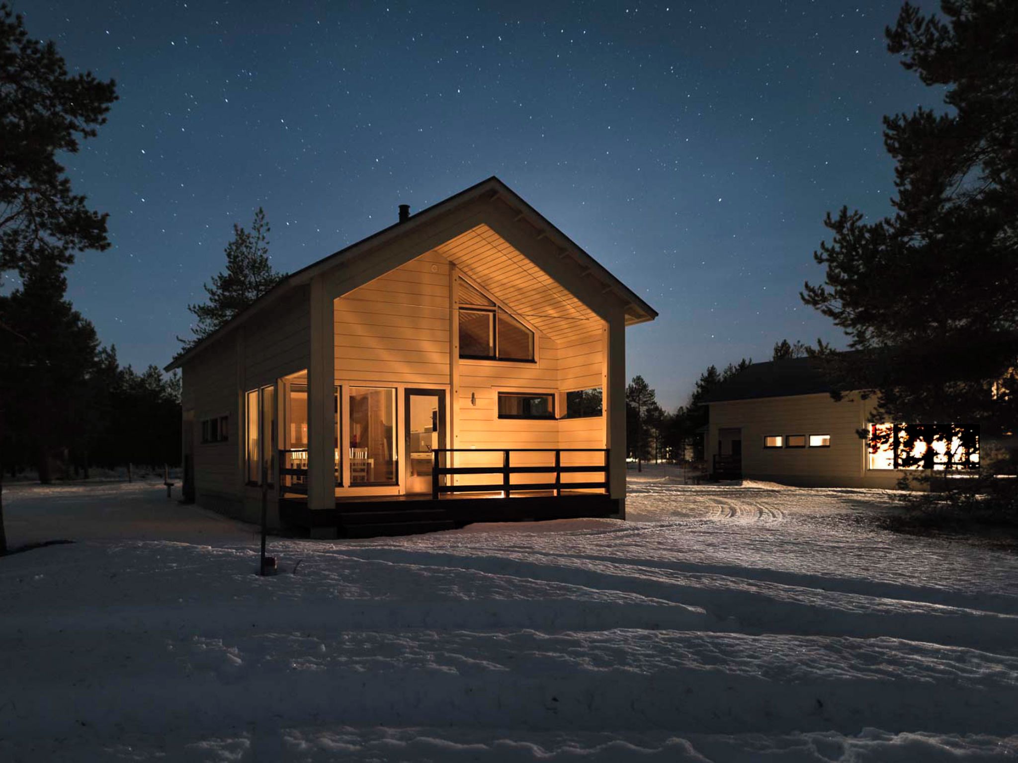 A wooden cabin with a porch, large windows, and a snow-covered ground.