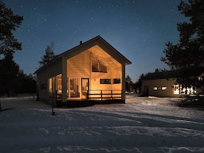 Une cabane en bois dotée d’un porche, de grandes fenêtres et dont le sol est recouvert de neige.