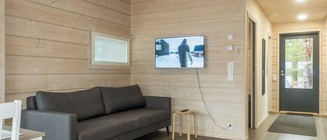 Un interior moderno con un sofá gris, un televisor montado en la pared y suelo de madera.