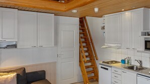 Un espace de vie compact comprenant un coin cuisine, une échelle en bois, un canapé et une petite table.