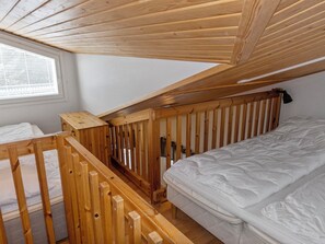 Quarto em dormitório com beliche, grades de madeira, janela com persianas e colchão branco.