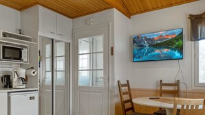 Une cuisine compacte équipée d’un four à micro-ondes, d’une machine à café et d’un petit réfrigérateur. Un coin repas avec une table et des chaises est à disposition, ainsi qu’un téléviseur fixé au mur qui diffuse des images de paysages pittoresques.