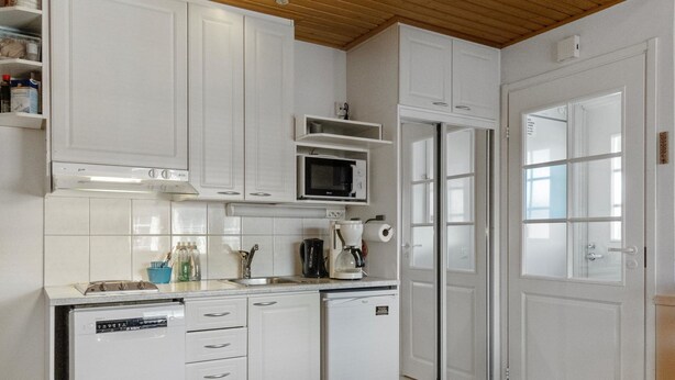Une cuisine moderne avec des meubles blancs, un four à micro-ondes encastré, une machine à café et un lave-vaisselle.