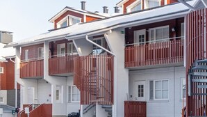 Un immeuble à plusieurs étages, doté de balcons, d’un escalier et d’une voiture garée devant.