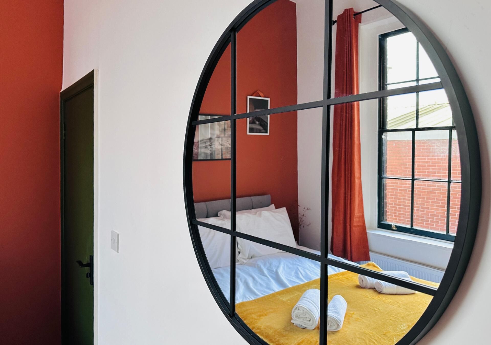 A circular window view of a bedroom with a bed, a small picture frame, and a window with curtains.