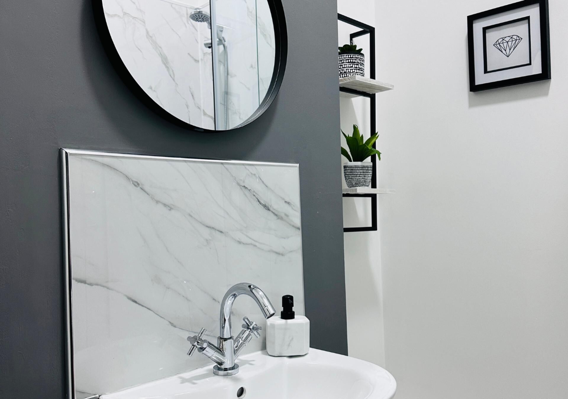 A bathroom with a marble sink, a round mirror, and a black-framed diamond picture on the wall.