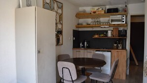 Een compacte keuken met een magnetron, broodrooster en koffiezetapparaat. Er is een eettafel met vier stoelen en een klein krukje.