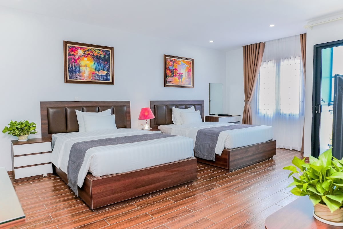 Une chambre d’hôtel avec deux lits, une table de chevet avec une lampe, une plante en pot et des œuvres d’art accrochées aux murs.