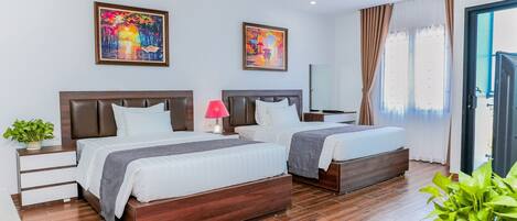 Quarto de hotel com duas camas, uma mesa de cabeceira com abajur, uma planta em vaso e obras de arte nas paredes.