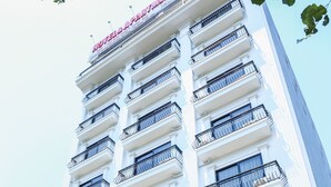 Un hôtel à plusieurs étages doté de balcons, une pancarte indiquant qu’il faut marcher 10 minutes pour rejoindre un restaurant à proximité, et une voiture garée devant.