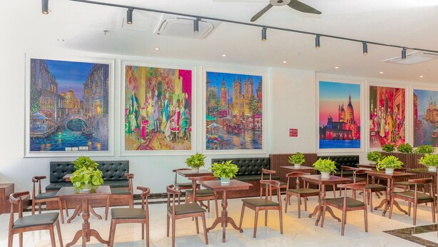 Un espace repas avec des tables et des chaises en bois, un canapé en cuir noir et de grandes peintures accrochées au mur.