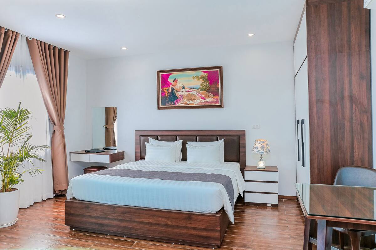 Une chambre d’hôtel moderne avec un grand lit, des tables de chevet, un bureau et un tableau au mur.