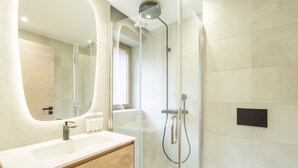 A modern bathroom with a glass-enclosed shower, a wooden vanity with a sink, and a large mirror.