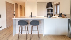 A modern kitchen with a central island, two bar stools, a built-in oven, and a window.