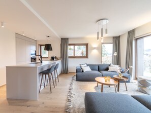 A modern living space with a kitchen area, a grey sofa, a coffee table, and a view of the outdoors. - Modern apartment in Courchevel Le Praz center with Wifi and parking (Courchevel)