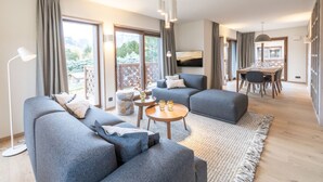 A modern living room with grey sofas, a round coffee table, and a dining area with a wooden table and chairs.