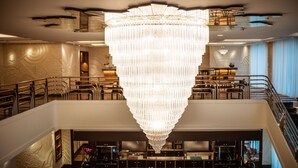 A spacious hotel lobby with a large chandelier, a staircase, and a bar area.