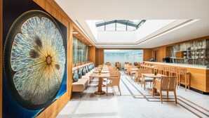 A modern restaurant with a large decorative wall, wooden furniture, and a high ceiling with skylights.