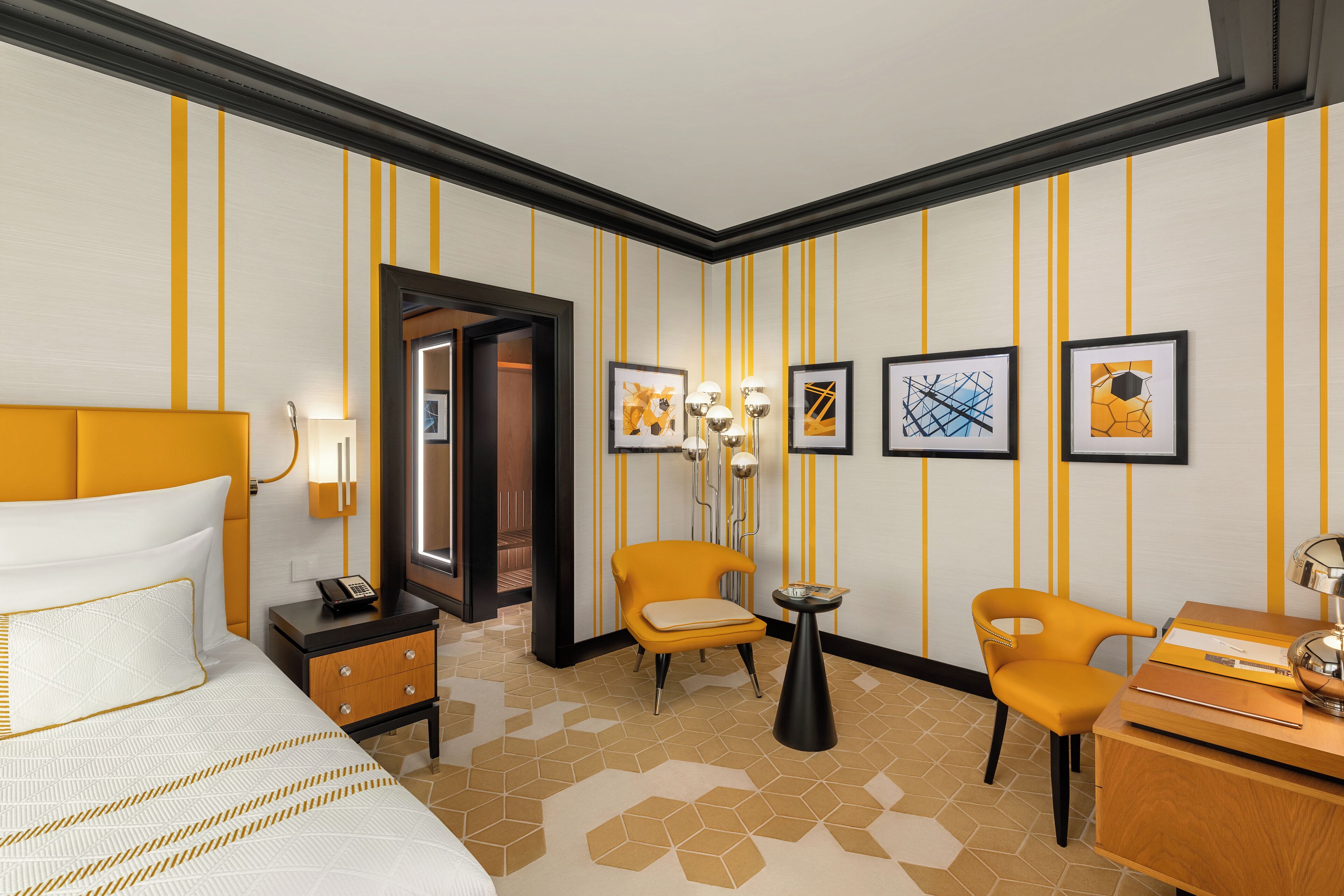 Une chambre d’hôtel avec un lit, deux chaises, un bureau, une lampe et des œuvres d’art encadrées accrochées au mur.