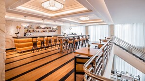 A modern hotel lobby with a bar area, wooden flooring, and a staircase.