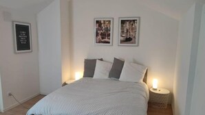 A bedroom with a bed, two bedside tables, and three framed pictures on the wall.