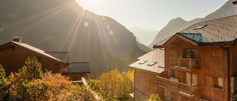 A wooden cabin with a balcony, surrounded by autumn foliage and mountains in the background.