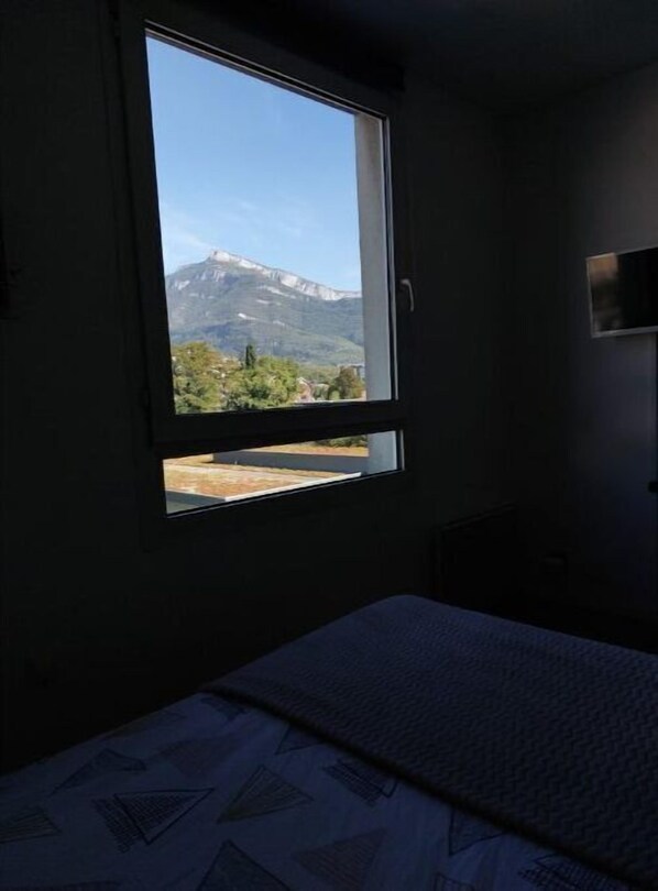 Enjoy breathtaking views of the surrounding mountains from the comfort of this room, featuring a cozy bed and a bedside table.