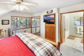 Ein Schlafzimmer mit einem Bett, einem an der Wand montierten Fernseher, einem Deckenventilator und einem Fenster mit Jalousien.