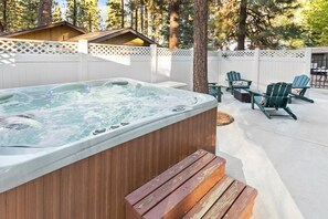 Ein Whirlpool mit einer Holzterrasse, umgeben von Adirondack-Stühlen und einem weißen Zaun.
