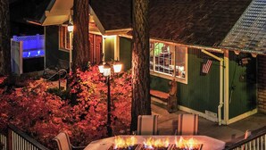 A cozy outdoor seating area with a fire feature, surrounded by trees and a building with a welcoming sign.
