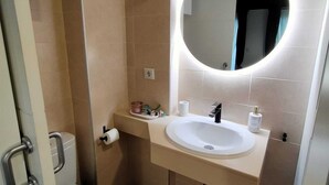 Ein modernes Badezimmer mit einem weißen Waschbecken, einem runden Spiegel und einer Toilette.