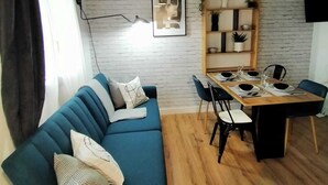 Ein modernes Wohnzimmer mit einem blauen Sofa, einem Esstisch für vier Personen und einer Wand aus weißen Ziegelsteinen.
