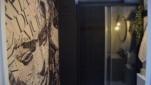 A bathroom with a glass shower enclosure, a towel hanging on the wall, and a decorative wall with various texts and images. - Apto 41. Residencial Alcoy (Alcoi)