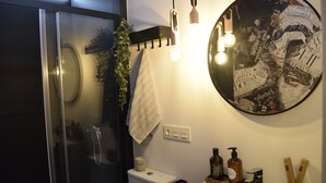 A modern bathroom with a glass shower enclosure, a toilet, a sink with toiletries, and a wall-mounted mirror with a decorative frame. - Apto 41. Residencial Alcoy (Alcoi)