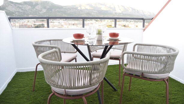 A balcony with a round table, four wicker chairs, and a view of a city and mountains. - Apto 41. Residencial Alcoy (Alcoi)