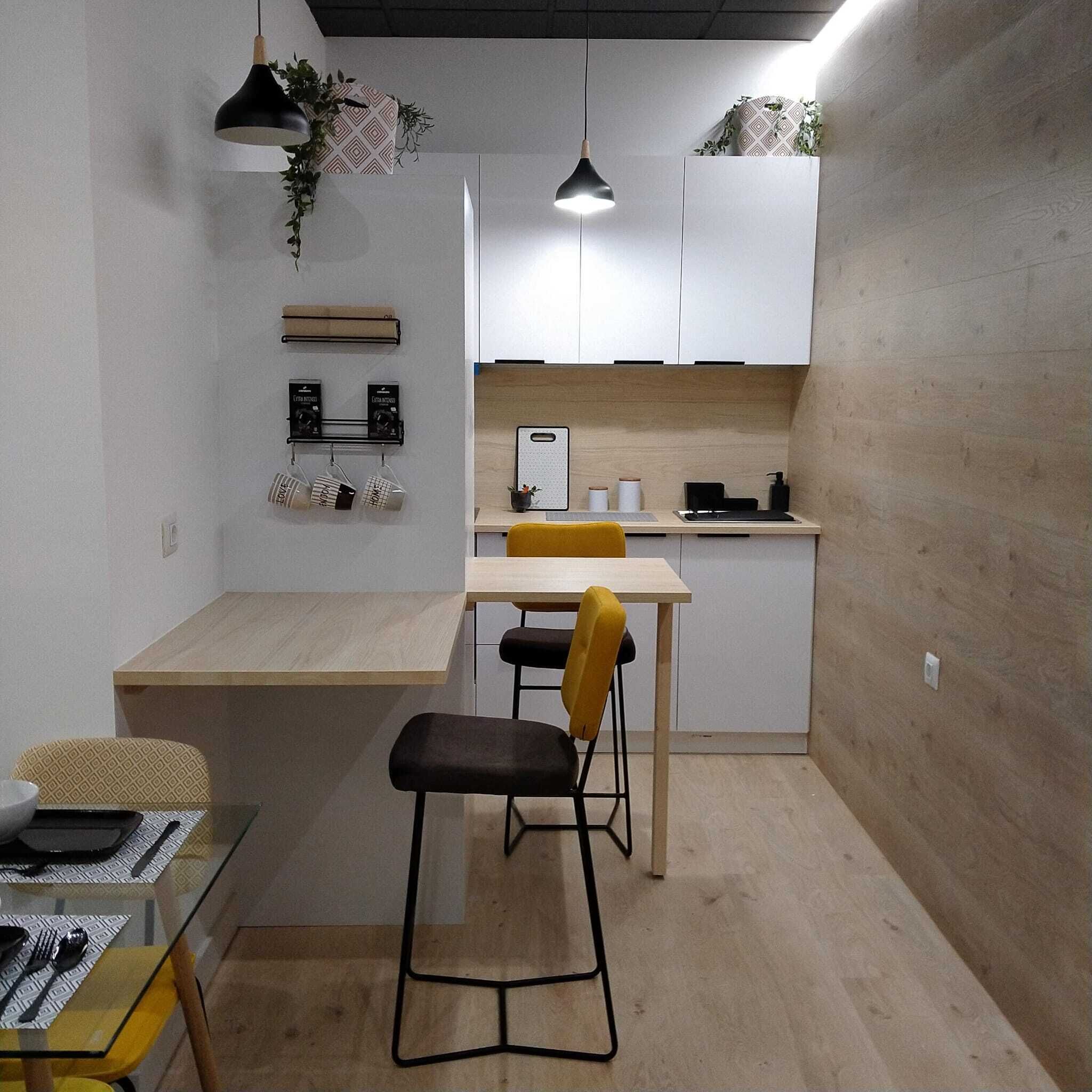 A compact kitchen with a dining area, a bar stool, and a hanging pendant light.