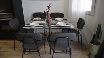 Een eethoek met een tafel voor vier personen, omringd door stoelen, een bloevas en een cactus.