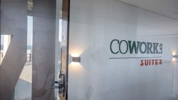 A glass door with a reflection of a person and a chair, and a wall with the text "COWORK: SUITES".