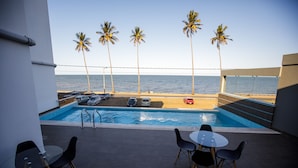 A pool area with a view of the beach and ocean, featuring palm trees, lounge chairs, and a pool table. - Cowork Lab Suites (Maputo)